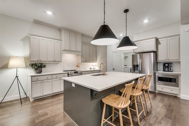 kitchen with a center island with sink, appliances with stainless steel finishes, dark hardwood / wood-style flooring, pendant lighting, and washing machine and clothes dryer