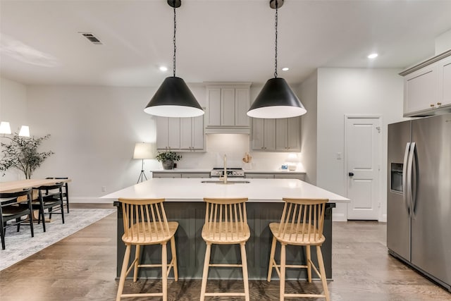 kitchen with wood finished floors, visible vents, an island with sink, stainless steel fridge with ice dispenser, and light countertops