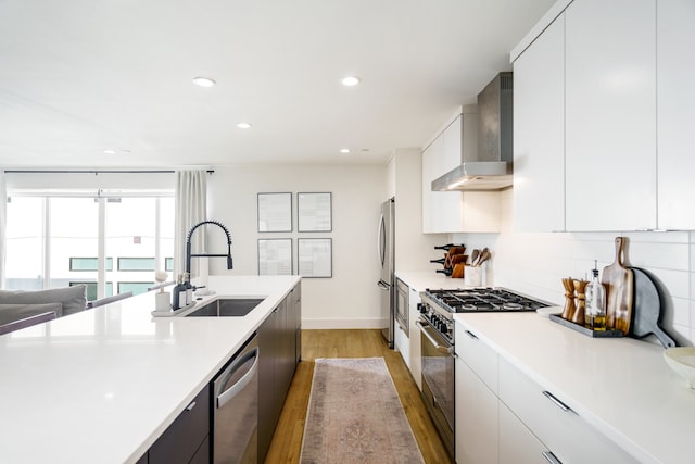 kitchen with white cabinetry, light wood-type flooring, appliances with stainless steel finishes, and wall chimney exhaust hood