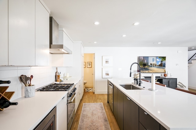 kitchen featuring white cabinetry, sink, appliances with stainless steel finishes, light hardwood / wood-style flooring, and wall chimney range hood