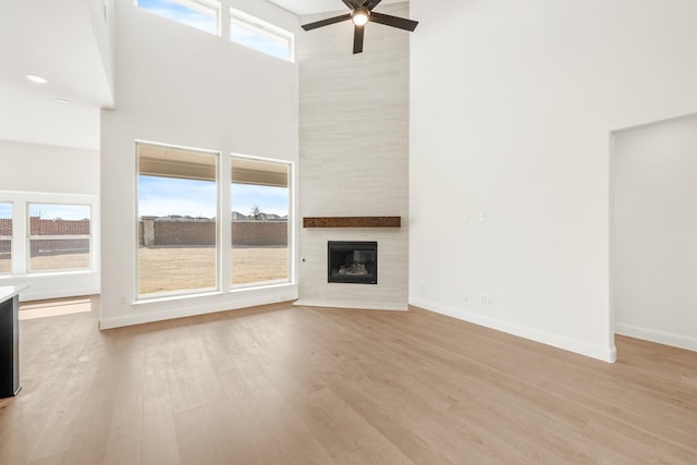 unfurnished living room featuring a high ceiling, a fireplace, baseboards, and wood finished floors