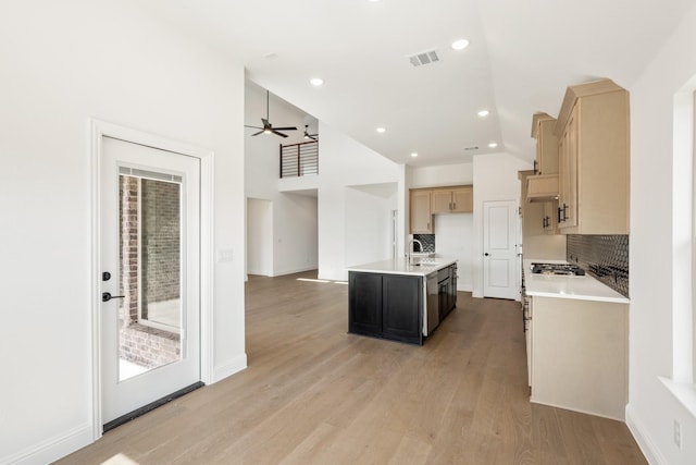 kitchen featuring visible vents, light countertops, light wood finished floors, an island with sink, and tasteful backsplash