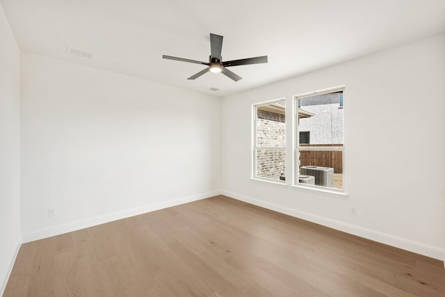 spare room with a ceiling fan, wood finished floors, visible vents, and baseboards