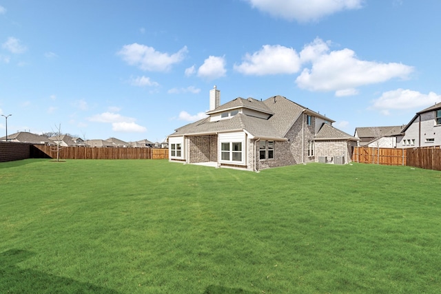 rear view of house featuring brick siding, a fenced backyard, a chimney, and a yard