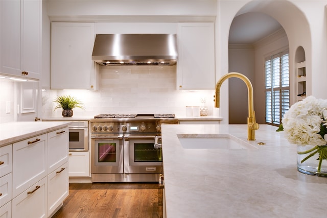 kitchen featuring white cabinets, light hardwood / wood-style floors, wall chimney range hood, and range with two ovens