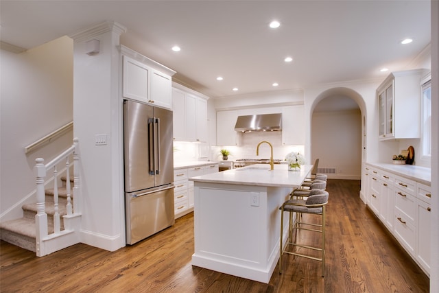 kitchen featuring high end fridge, hardwood / wood-style flooring, wall chimney range hood, a breakfast bar, and white cabinetry