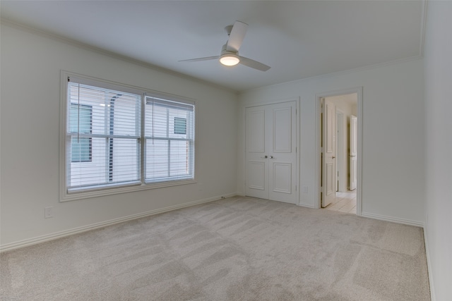 unfurnished bedroom featuring ceiling fan, light colored carpet, a closet, and crown molding