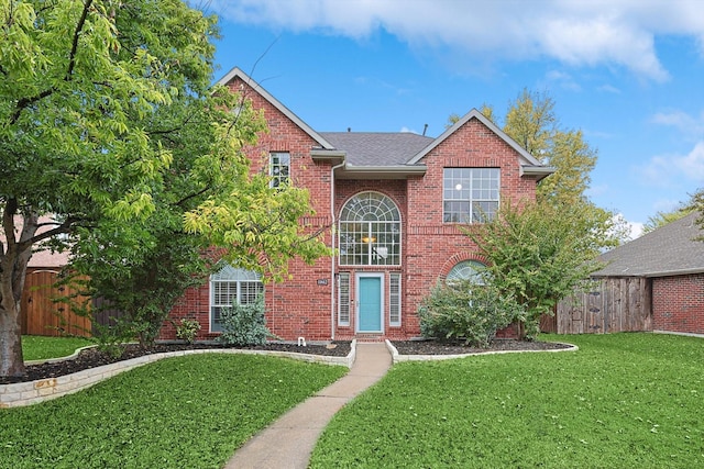 traditional-style home with brick siding, a shingled roof, fence, and a front yard