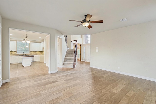 unfurnished living room with visible vents, stairway, light wood-style flooring, and baseboards