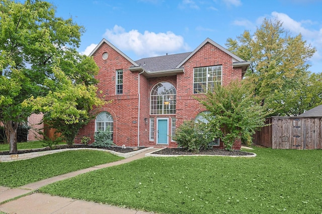 traditional-style house with roof with shingles, fence, a front lawn, and brick siding