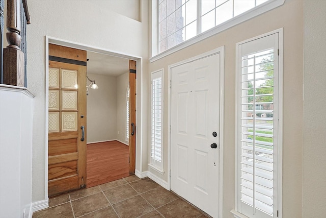 foyer entrance featuring a towering ceiling, baseboards, and dark tile patterned flooring