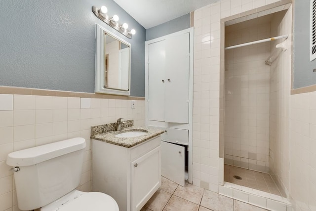 bathroom with toilet, vanity, tile walls, and a tile shower