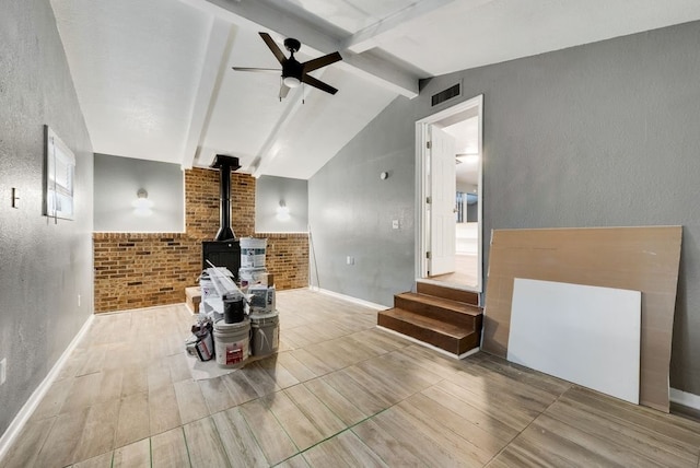 living room featuring brick wall, ceiling fan, hardwood / wood-style floors, a wood stove, and lofted ceiling with beams