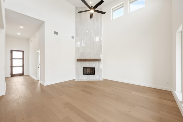 unfurnished living room with a high ceiling, a high end fireplace, ceiling fan, light wood-type flooring, and baseboards