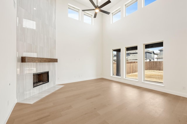 unfurnished living room with ceiling fan, a high ceiling, a fireplace, wood finished floors, and baseboards