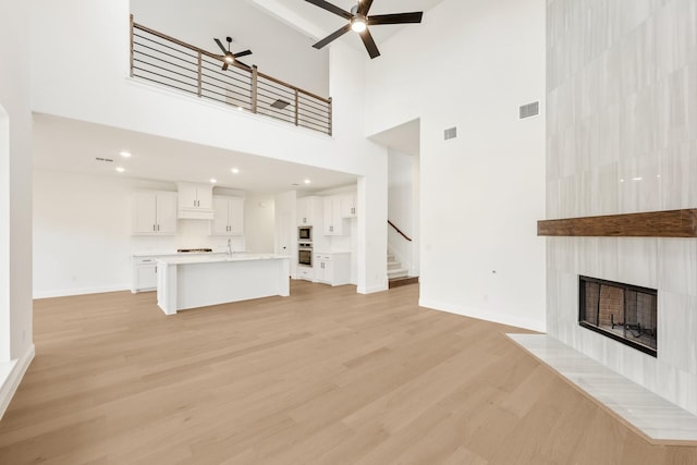 unfurnished living room with a tile fireplace, visible vents, a ceiling fan, stairs, and light wood-type flooring