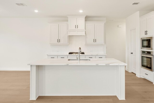 kitchen featuring a center island with sink, stainless steel appliances, sink, white cabinets, and light hardwood / wood-style flooring