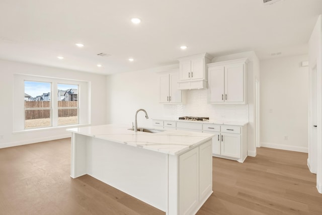 kitchen with light wood-style flooring, a kitchen island with sink, white cabinetry, a sink, and gas cooktop