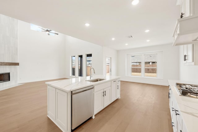 kitchen featuring a large fireplace, open floor plan, stainless steel appliances, light wood-style floors, and a sink