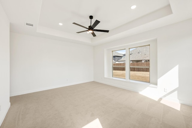 unfurnished room featuring a tray ceiling, light colored carpet, visible vents, and baseboards