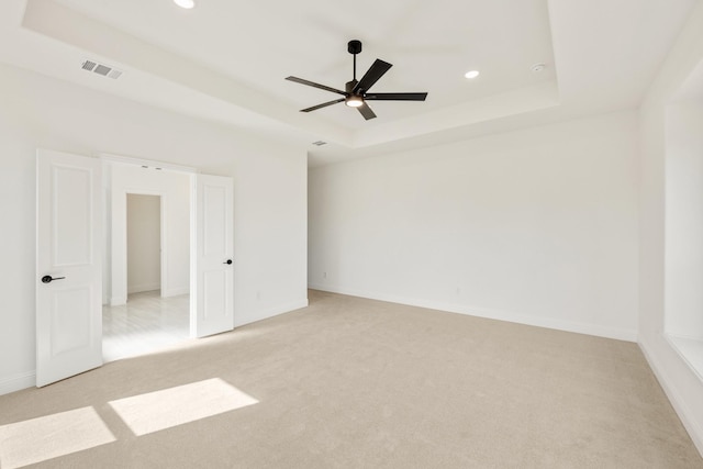 empty room featuring light carpet, visible vents, a tray ceiling, and baseboards