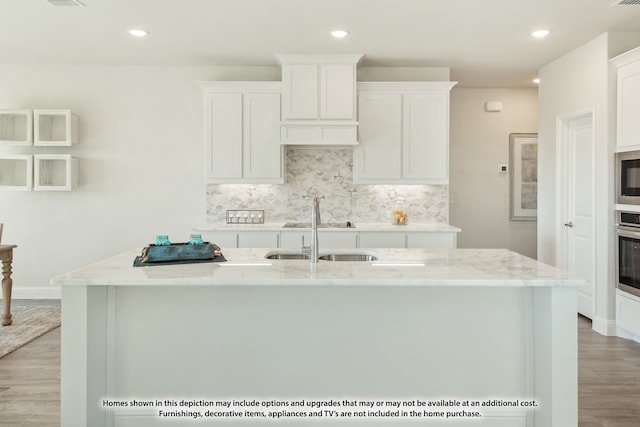 kitchen with white cabinetry, light wood-type flooring, an island with sink, and light stone countertops