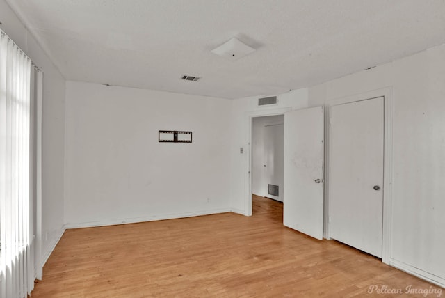 unfurnished bedroom featuring a textured ceiling, light wood-type flooring, and multiple windows