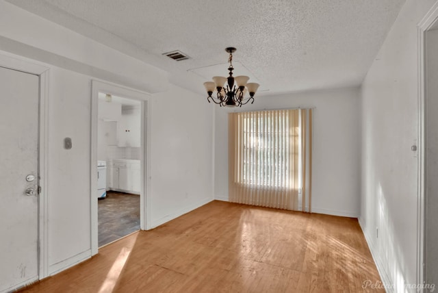 spare room featuring hardwood / wood-style floors, a notable chandelier, and a textured ceiling