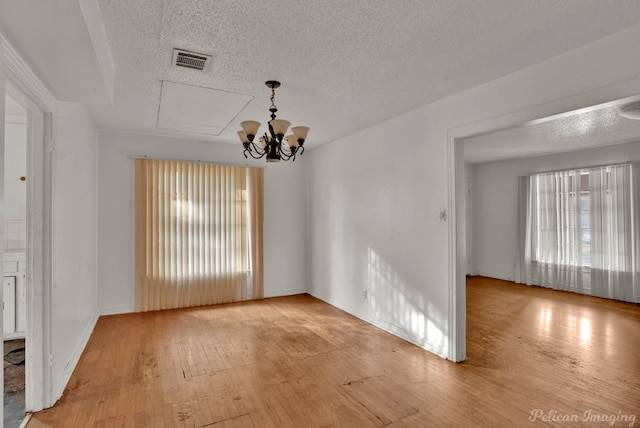 spare room featuring an inviting chandelier, a textured ceiling, and light hardwood / wood-style flooring