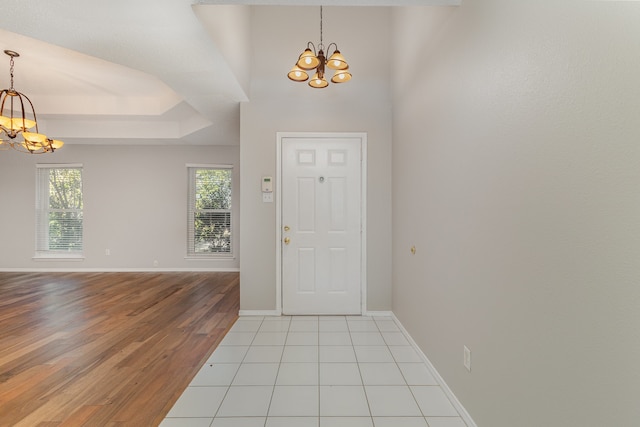 foyer with light hardwood / wood-style floors, an inviting chandelier, plenty of natural light, and a tray ceiling