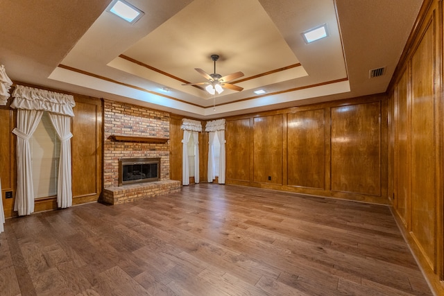 unfurnished living room featuring ceiling fan, a raised ceiling, wood-type flooring, and a brick fireplace