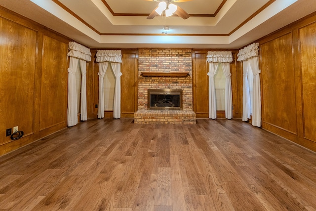 unfurnished living room featuring ornamental molding, a raised ceiling, ceiling fan, hardwood / wood-style flooring, and a fireplace