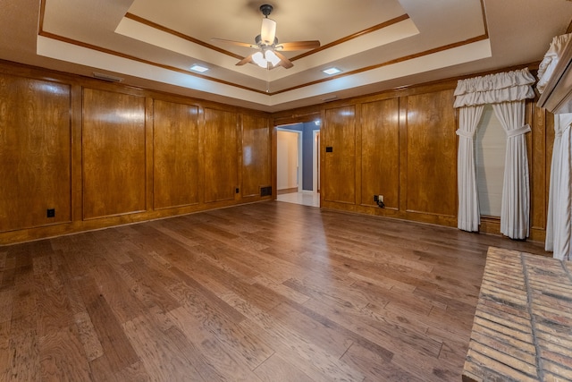 spare room featuring a raised ceiling, ceiling fan, wooden walls, and wood-type flooring