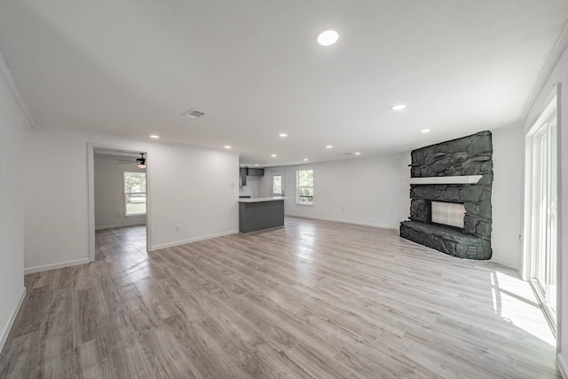 unfurnished living room featuring light hardwood / wood-style flooring, a fireplace, a wealth of natural light, and crown molding