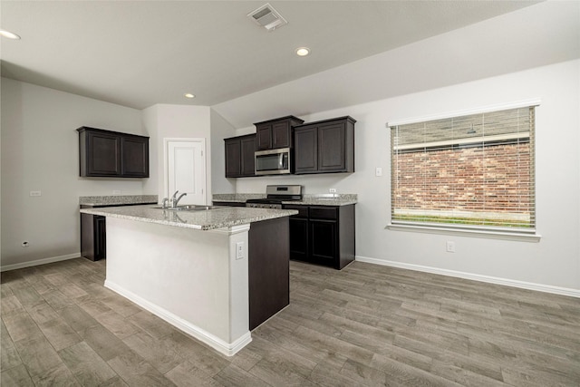 kitchen featuring a center island with sink, stainless steel appliances, light hardwood / wood-style flooring, sink, and light stone counters