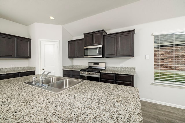 kitchen with appliances with stainless steel finishes, dark wood-type flooring, dark brown cabinetry, light stone countertops, and sink