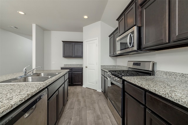 kitchen with light hardwood / wood-style floors, sink, light stone counters, and appliances with stainless steel finishes