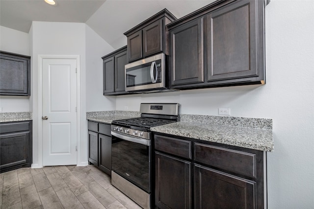 kitchen with dark brown cabinetry, light wood-type flooring, stainless steel appliances, and lofted ceiling