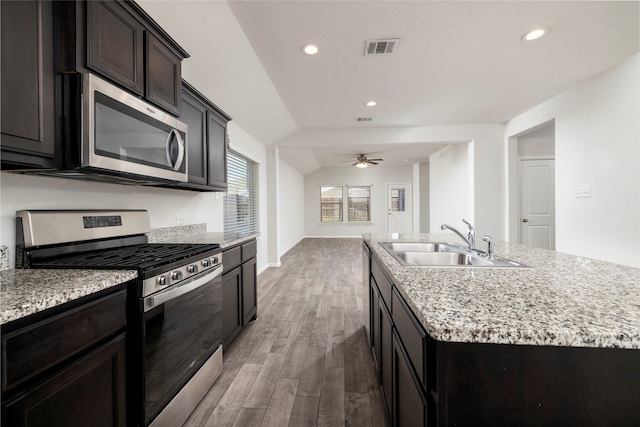 kitchen with stainless steel appliances, vaulted ceiling, sink, an island with sink, and light hardwood / wood-style floors