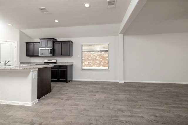 kitchen with light wood-type flooring, appliances with stainless steel finishes, light stone counters, and lofted ceiling