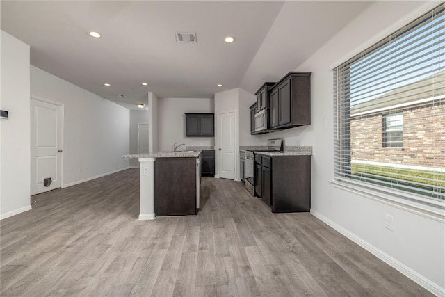 kitchen with appliances with stainless steel finishes, light hardwood / wood-style flooring, an island with sink, light stone countertops, and sink