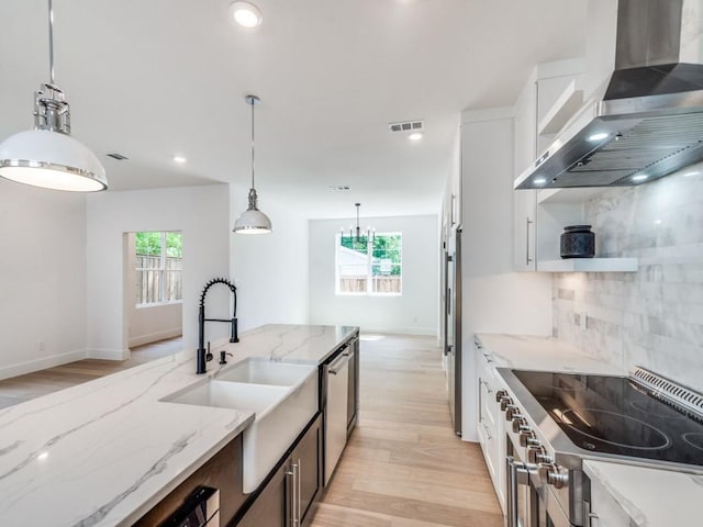 kitchen with light stone countertops, tasteful backsplash, wall chimney range hood, white cabinetry, and hanging light fixtures