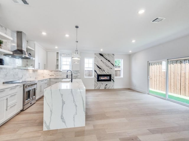 kitchen with white cabinetry, hanging light fixtures, wall chimney range hood, range with two ovens, and a fireplace