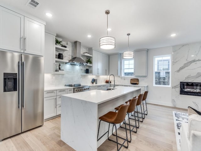 kitchen with a kitchen island with sink, wall chimney range hood, sink, decorative light fixtures, and stainless steel appliances