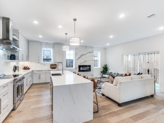 kitchen featuring appliances with stainless steel finishes, wall chimney exhaust hood, sink, white cabinets, and hanging light fixtures