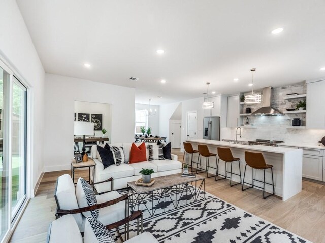 kitchen with sink, wall chimney exhaust hood, stainless steel range oven, decorative light fixtures, and a kitchen island with sink