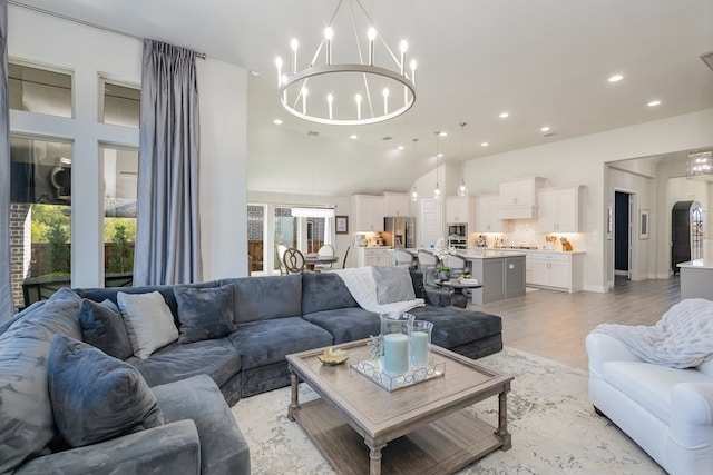 living room with a towering ceiling, a notable chandelier, and light wood-type flooring