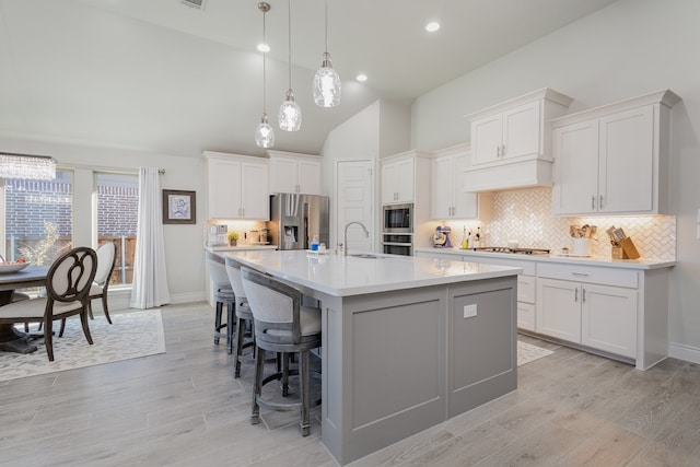 kitchen featuring high vaulted ceiling, white cabinets, light hardwood / wood-style flooring, an island with sink, and appliances with stainless steel finishes