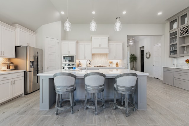 kitchen with a center island with sink, white cabinetry, stainless steel appliances, and hanging light fixtures