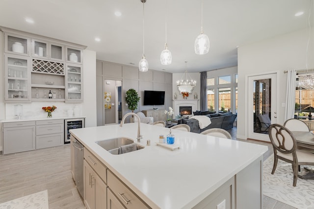 kitchen featuring sink, stainless steel dishwasher, pendant lighting, a center island with sink, and light wood-type flooring